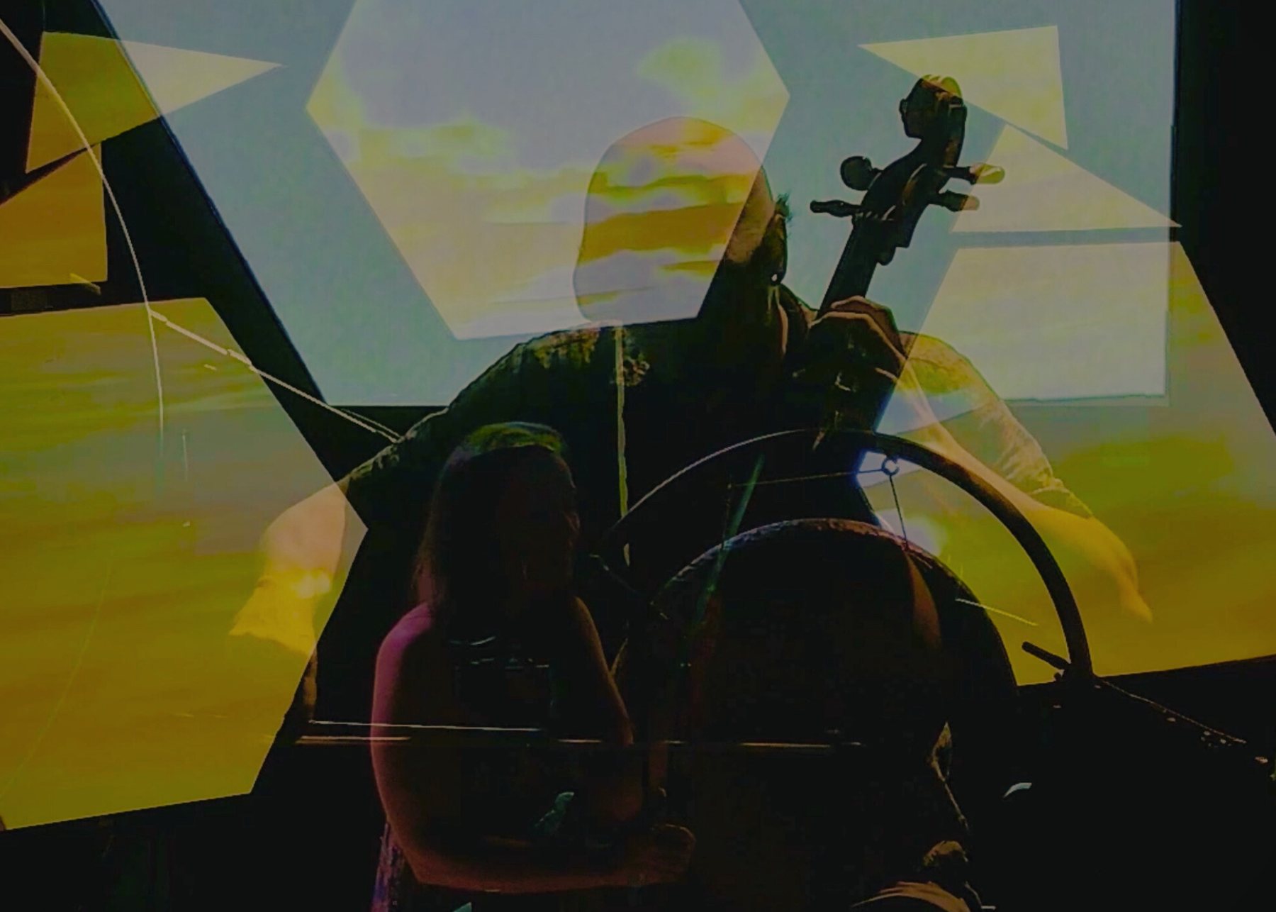 Taylor plays cello and Sariah sings as geometric projections in gold and blue layer over them at the Arts Council