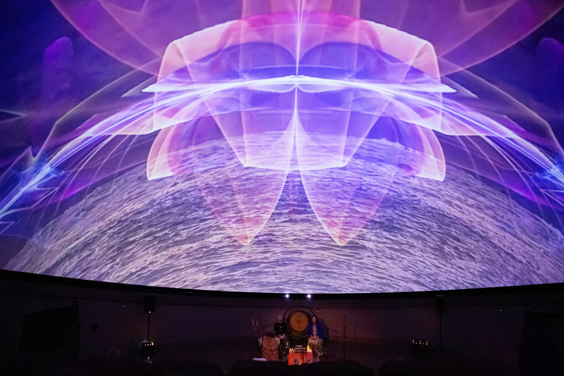 A luminous violet lotus unfolds over a sea of light across the dome as Sariah and Taylor perform below
