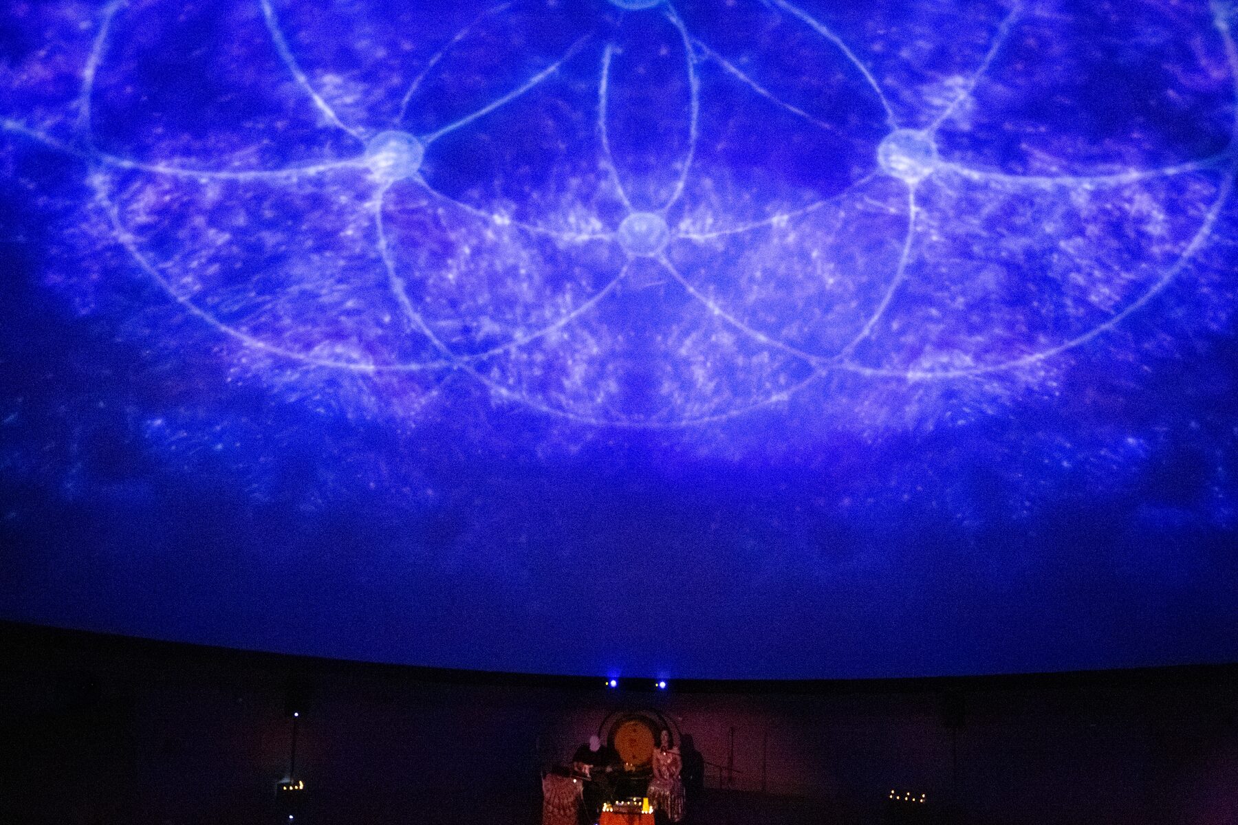 A flower-of-life pattern woven from stars spans the deep blue dome above the performers