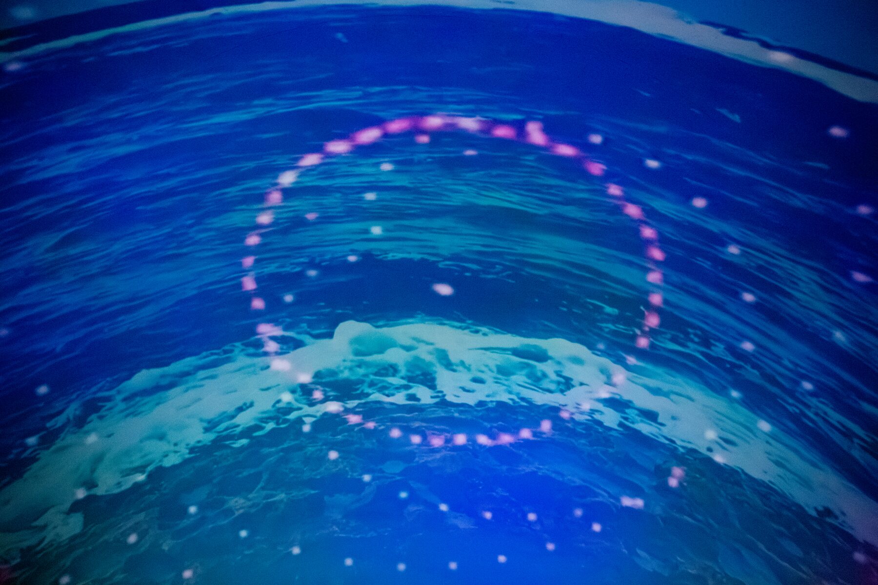 A ring of pink light floats over ocean waves projected across the dome