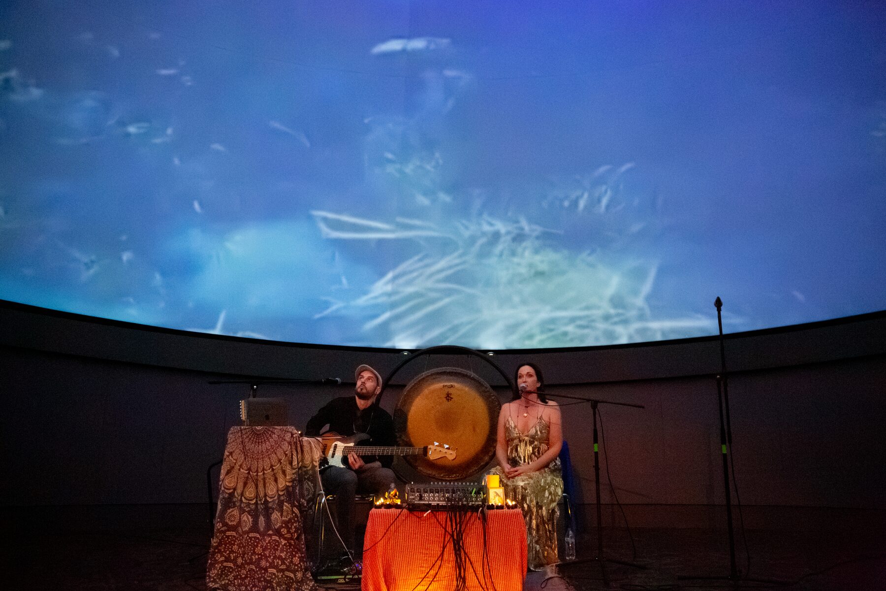 Sariah and Taylor perform with gong and candlelight beneath an underwater projection