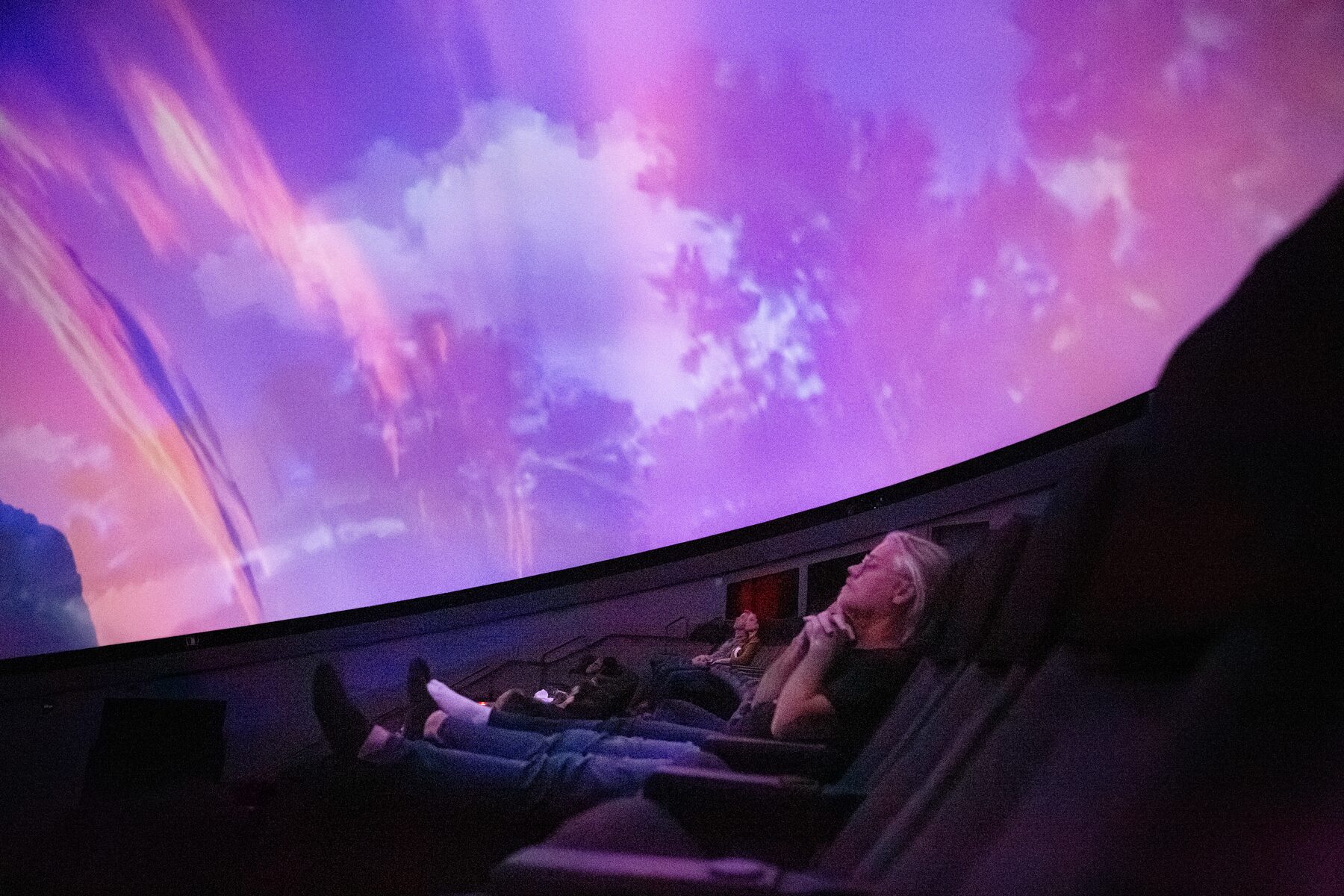 A guest rests with hands folded beneath glowing pink and violet clouds on the dome