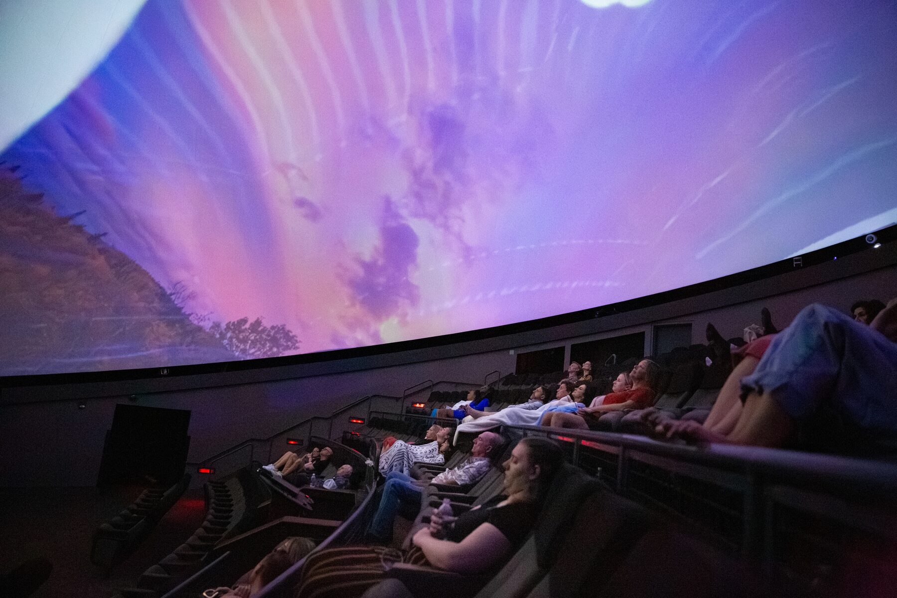 Rays of lavender and pink light stream across the dome above a reclining audience