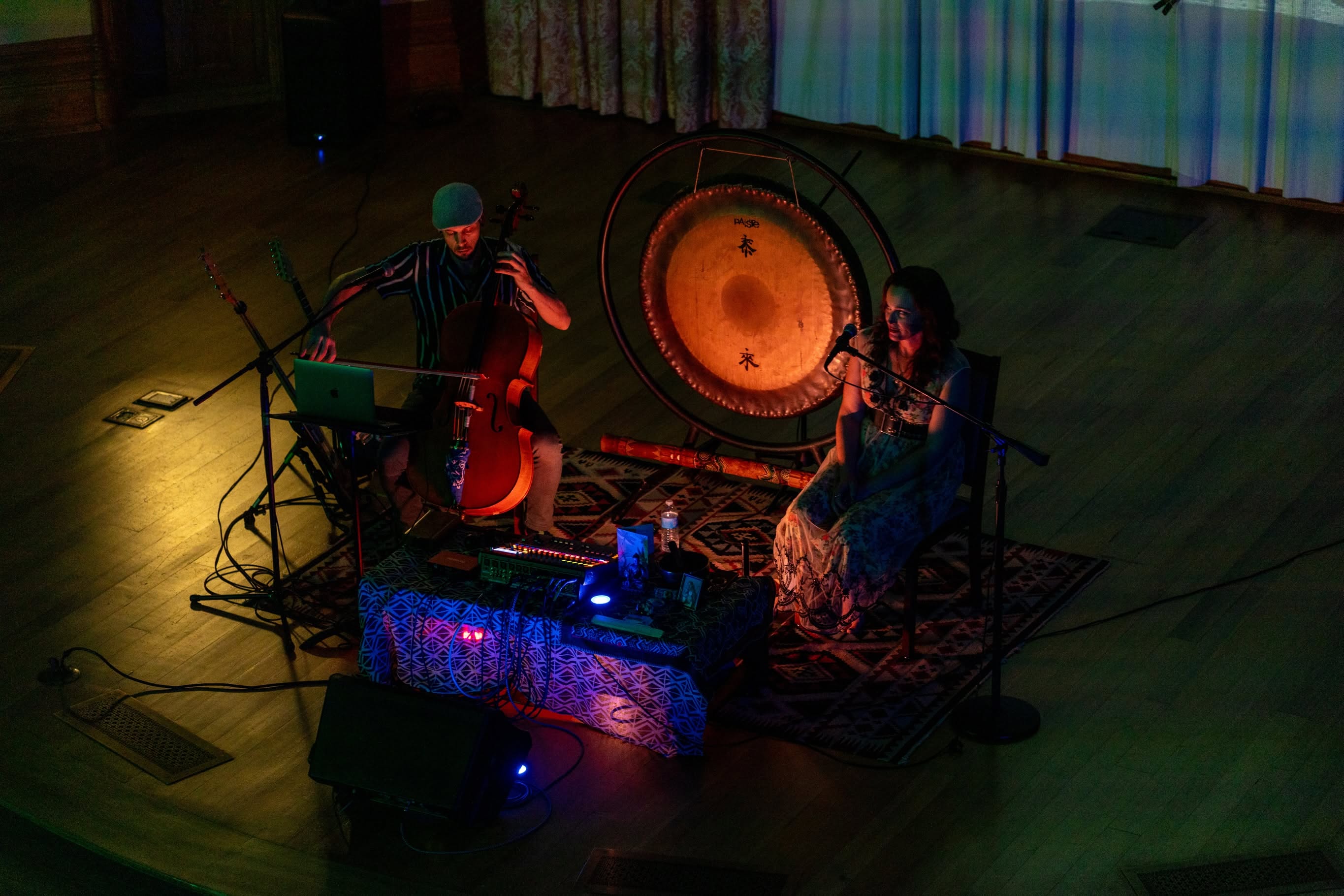 Taylor plays cello and Sariah sings beside the glowing gong, seen from the balcony
