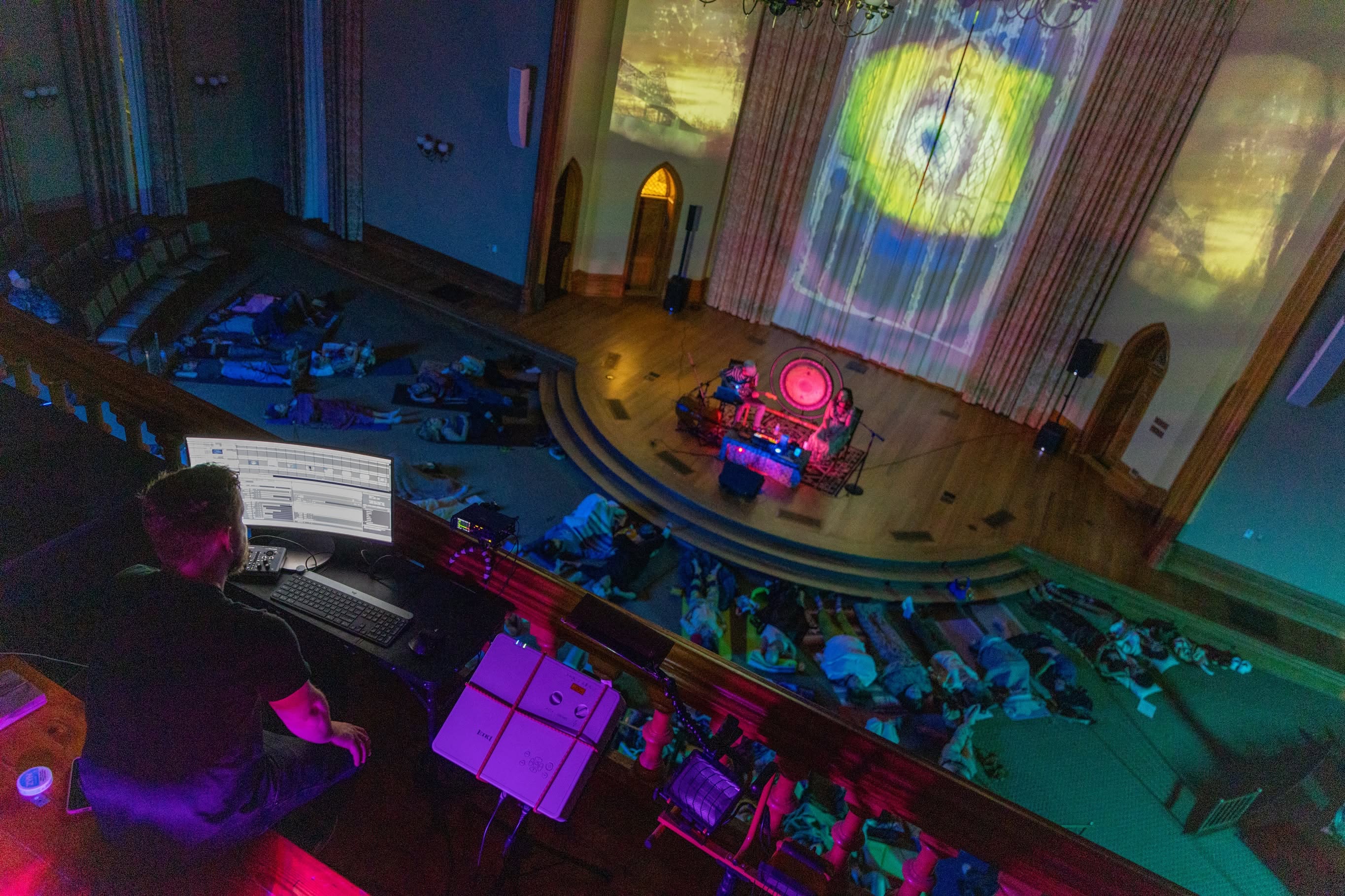 A swirling projection fills the stage wall above the performers as guests lie on the floor below