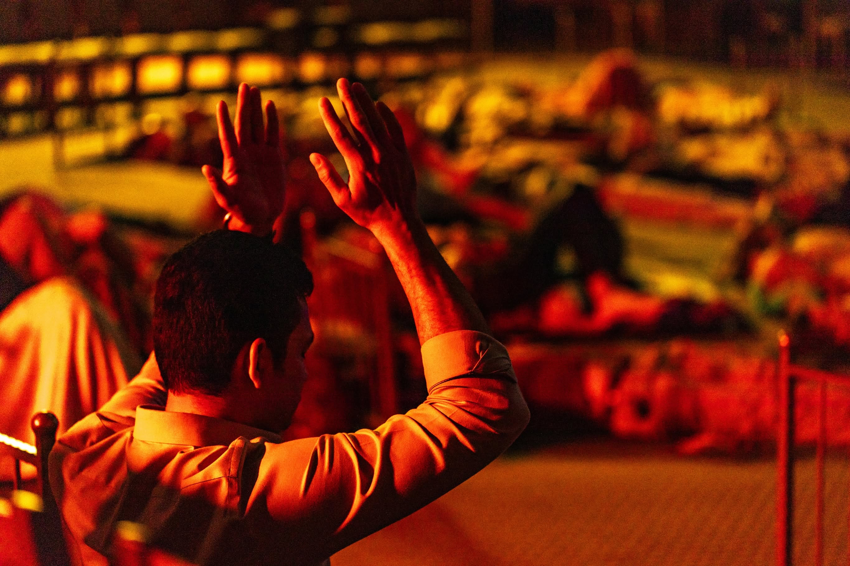 A guest raises both hands in amber light above the resting audience