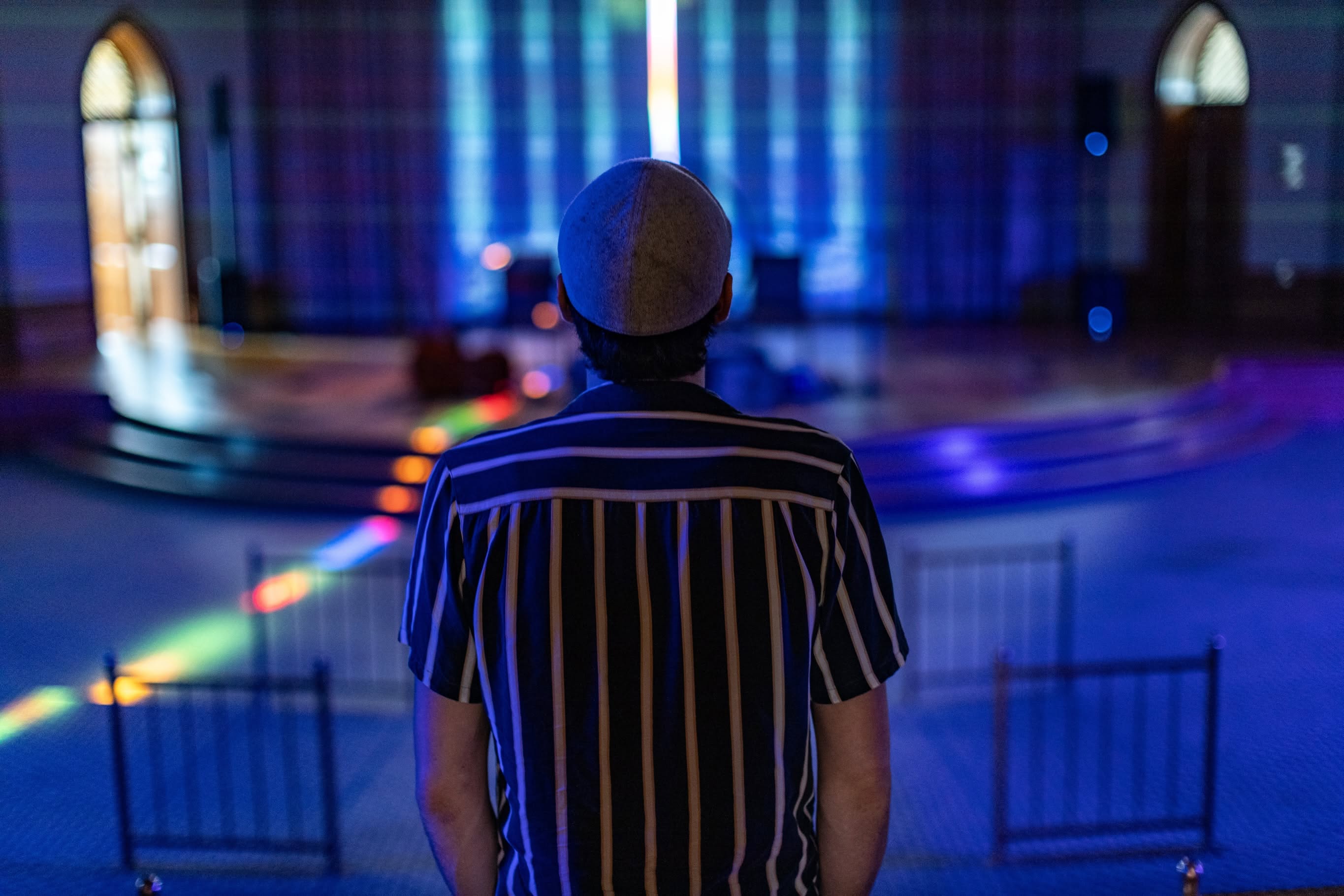 A guest in a striped shirt looks out over the chamber as rainbow light falls across the floor